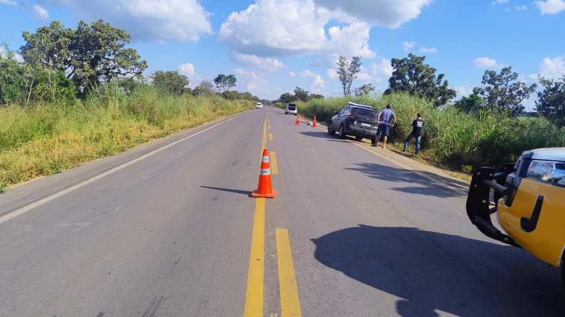 Vista de uma estrada com vegetação ao redor, carros estacionados e cones de sinalização ao longo da pista.