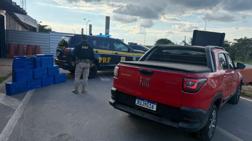 Imagem de uma abordagem da PRF com um carro vermelho da Fiat e um veículo da polícia. Há caixas azuis empilhadas à esquerda da imagem.