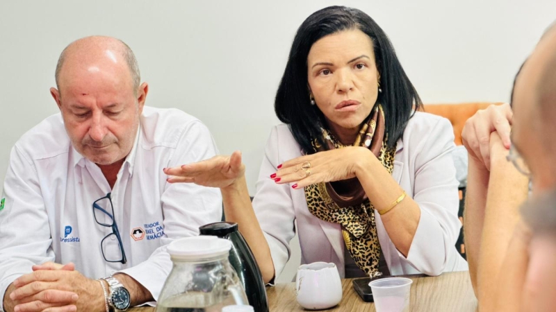 Duas pessoas participando de uma reunião, uma mulher falando com as mãos gesticulando enquanto um homem ao lado escuta.