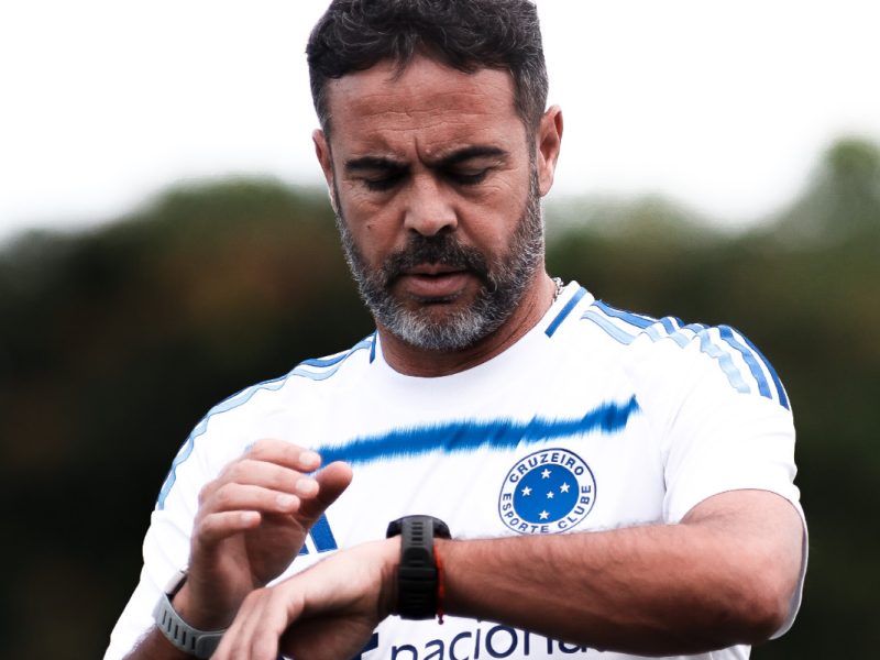 A man in a sports jersey is looking at a smartwatch on his wrist, in an outdoor setting.