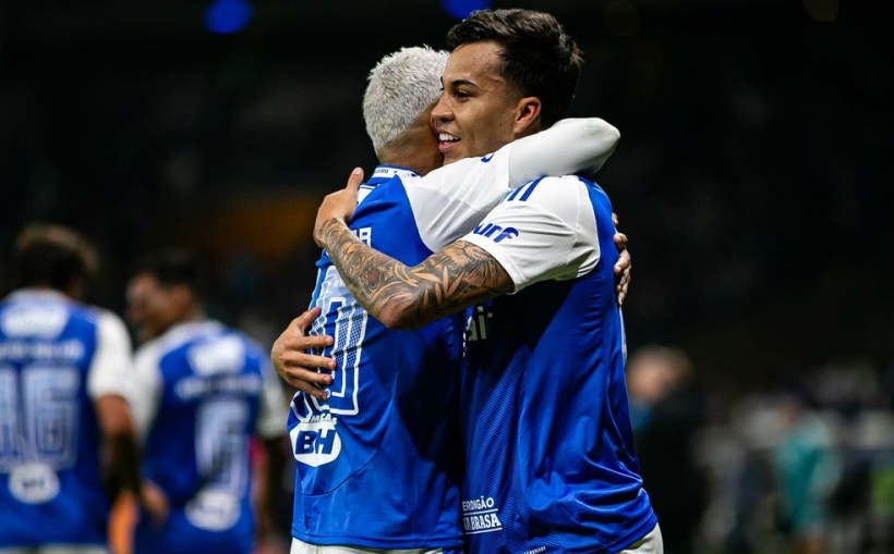 Two soccer players embrace happily after a match, both wearing blue and white team jerseys.