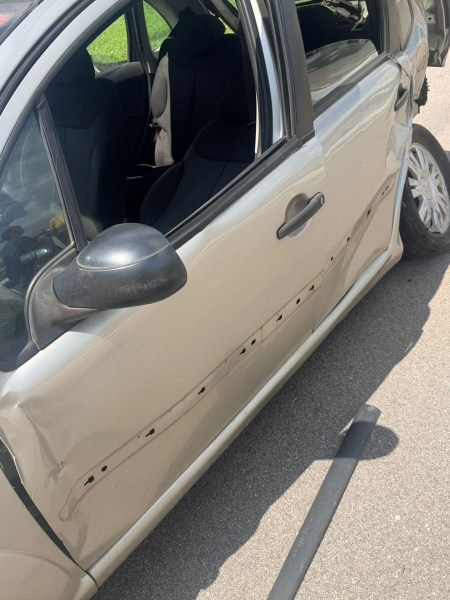 Imagem de um carro com a porta do lado esquerdo amassada e riscos visíveis na lataria. O interior do carro é visível, com bancos pretos.