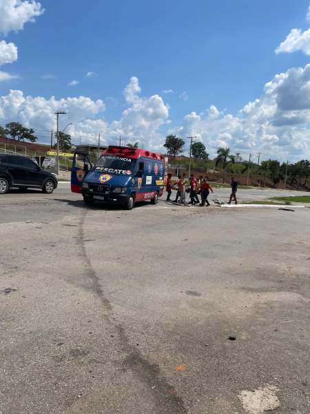 Uma ambulância vermelha estacionada em uma área aberta, com equipe de resgate se aproximando enquanto um carro preto está ao fundo.