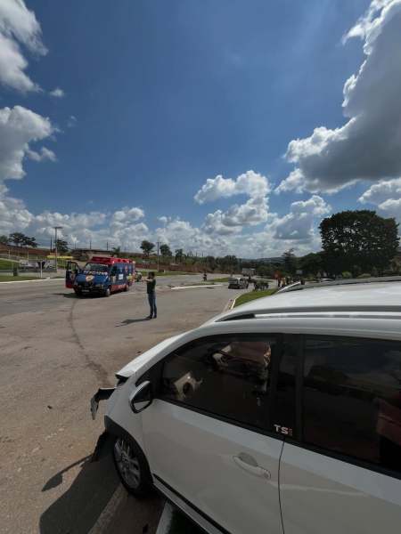 Vista de um acidente de carro na estrada, com um veículo branco em primeiro plano e um caminhão de bombeiros ao fundo sob um céu azul com nuvens.