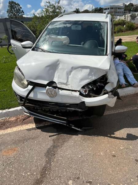 Carro branco danificado na frente, com capô amassado e faróis quebrados, estacionado em uma calçada.