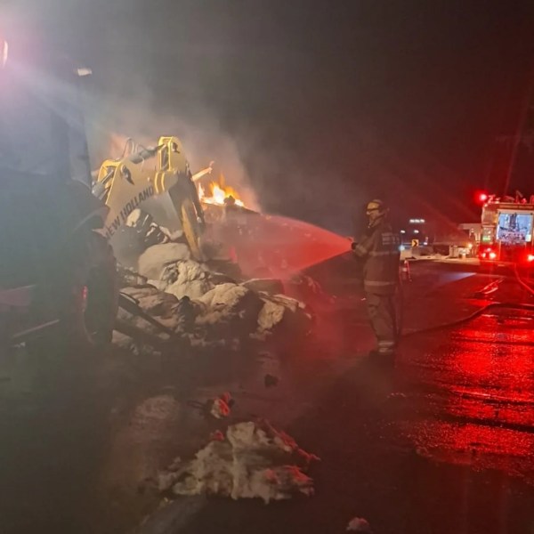 Bombeiros combatendo incêndio em uma pilha de materiais à noite, com uma retroescavadeira ao fundo.