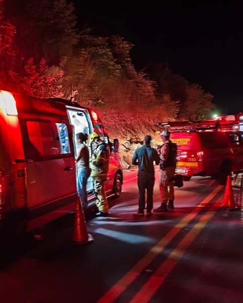 Equipe de emergência discutindo em uma estrada à noite, com viaturas de resgate e iluminação vermelha.