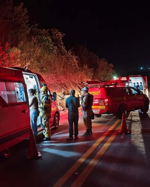 Equipe de resgate em ação à noite, com viaturas de emergência e pessoas conversando na estrada.