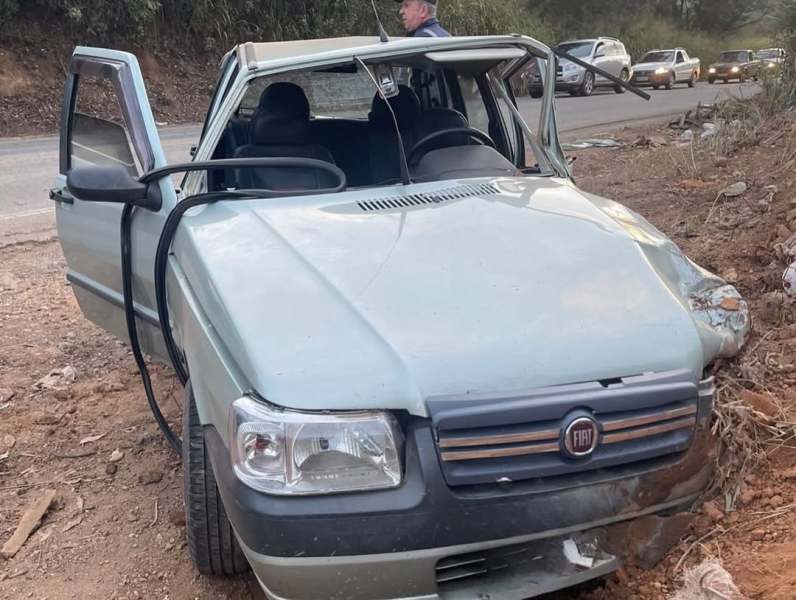 Carro Fiat danificado, com as portas abertas, estacionado em um terreno na beira da estrada.