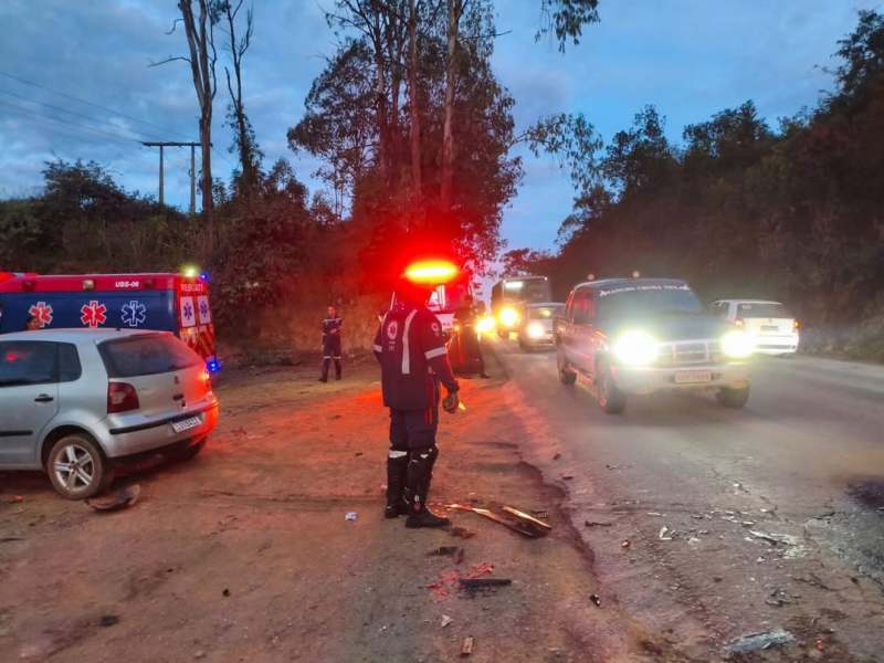 Cena de um acidente de trânsito com veículos envolvidos, incluindo uma ambulância. Há um profissional de emergência assistindo ao local, enquanto veículos estão parados na estrada ao entardecer.