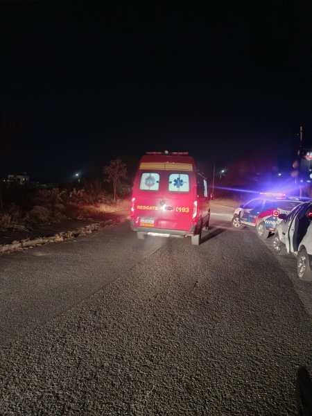 Uma ambulância vermelha estacionada em uma estrada à noite, com luzes piscando e veículos ao redor.