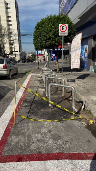 Ciclofaixa com paraciclos danificados e sinalização de interdição em área urbana.