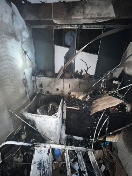 Interior de um espaço danificado por fogo, com paredes e objetos queimados e em desordem.