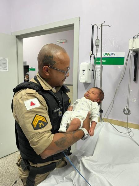 Policial segurando um bebê em um ambiente hospitalar.