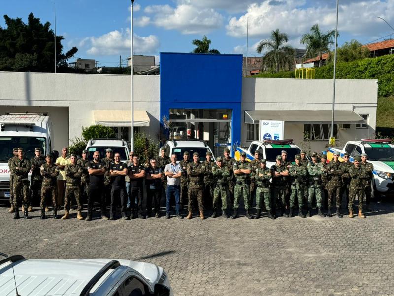 Grupo de militares e civis em frente a um edifício, posando em formação, com veículos estacionados ao fundo.