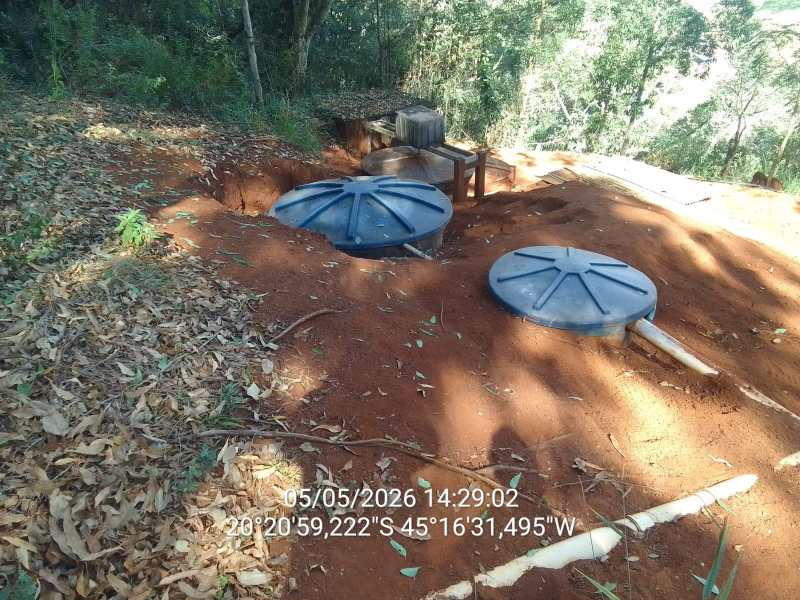 Tanques de armazenamento subterrâneo visíveis em um terreno de terra vermelha cercado por vegetação.