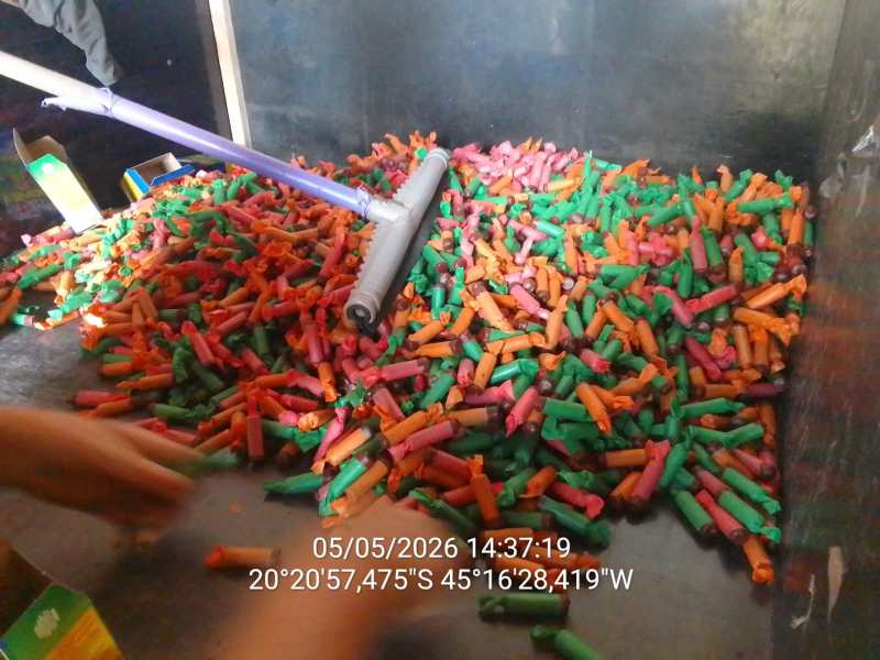 Uma grande pilha de pequenos objetos coloridos em um recipiente, com predominância de cores laranja, verde e rosa, e um rolo de tinta ao centro.