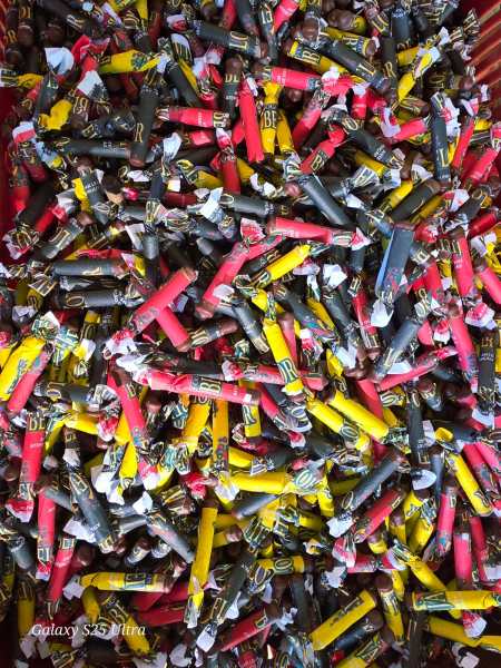 Uma pilha colorida de embalagens de bombons, em várias cores como vermelho, amarelo e preto, dispostas de forma aleatória.