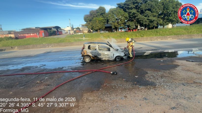 Um carro pegando fogo na estrada com um bombeiro apagando o incêndio em Formiga, MG.