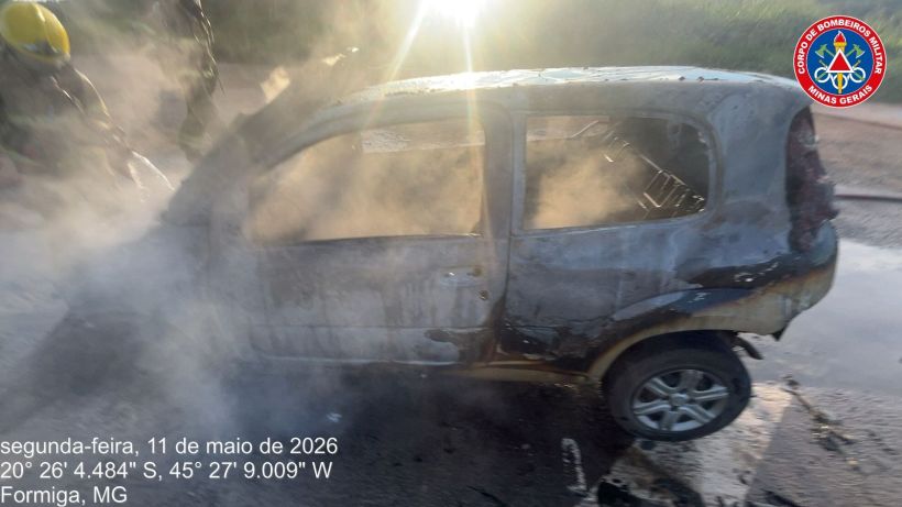 Carro parcialmente queimado em um acidente, com fumaça saindo do veículo, em Formiga, MG.