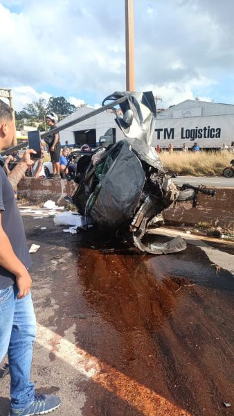 Carro acidentado virado na estrada, com pessoas observando ao redor.