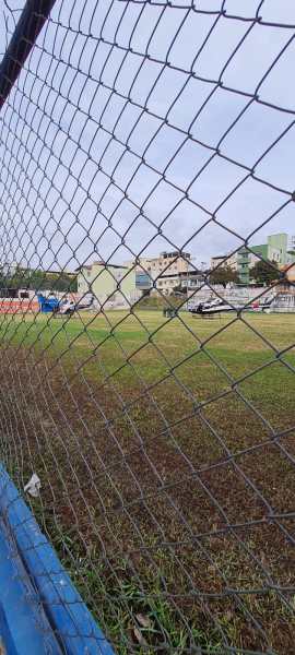 Vista de um campo de futebol em um bairro urbano, com uma rede de proteção em primeiro plano.