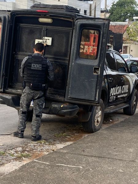 Agente da polícia civil abrindo a parte de trás de uma viatura de transporte de presos.