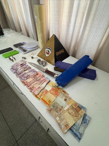 Mesa com objetos apreendidos incluindo dinheiro em notas, uma faca, balança e outros itens.