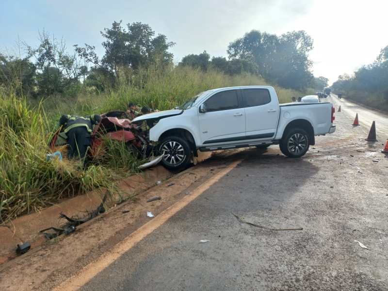 Acidente de carro na estrada, com uma caminhonete branca colidida em um veículo vermelho, enquanto socorristas prestam ajuda.