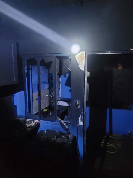 Interior de um cômodo danificado, com paredes azuis e escuras, movidos por uma fonte de luz.