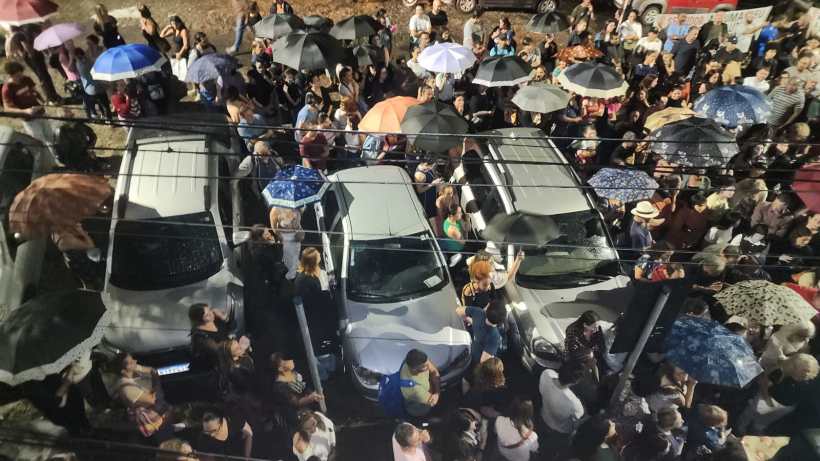 Multidão de pessoas com guarda-chuvas, cercando carros estacionados em um evento noturno.