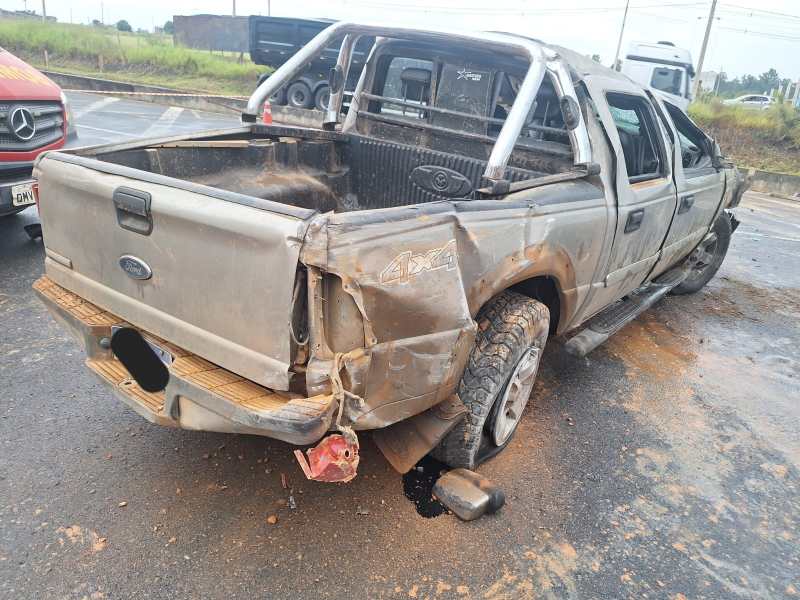 imagem de uma caminhonete Ford danificada, com parte traseira amassada e suja, parada em uma estrada, ao lado de outros veículos