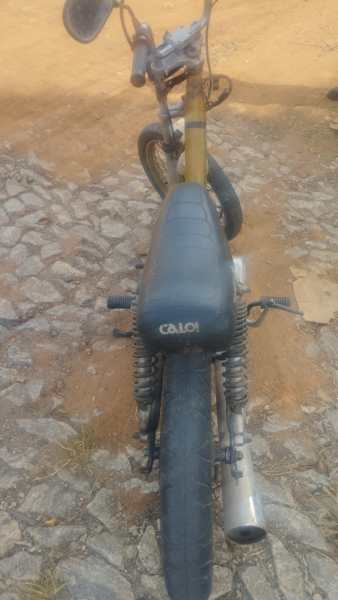 Vista traseira de uma bicicleta Caloi com assento preto e guidão visível, em um terreno de pedra e terra.