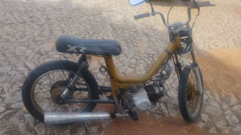 Uma bicicleta motorizada amarelo-escura com assento preto, rodas de aro fino e detalhes metálicos, parada em uma superfície de pedras.