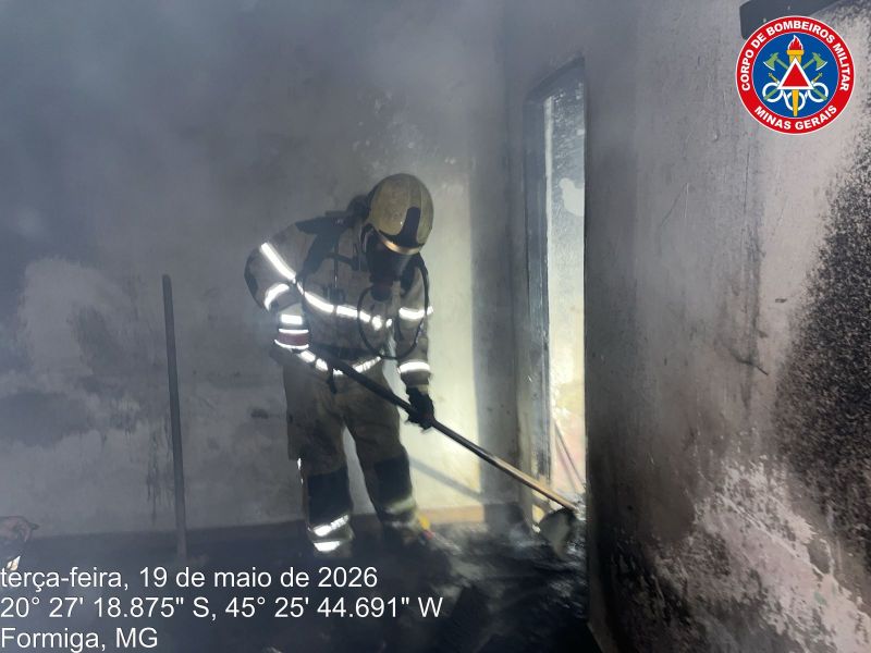Bombeiro combatendo fogo em um ambiente com fumaça, usando equipamento de proteção, em Formiga, MG, Brasil.