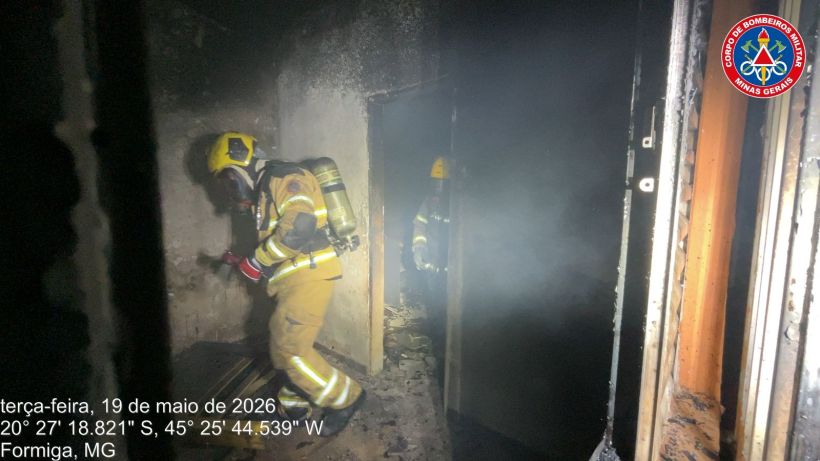 Bombeiros em operação de combate a incêndio em um ambiente danificado e cheio de fumaça.