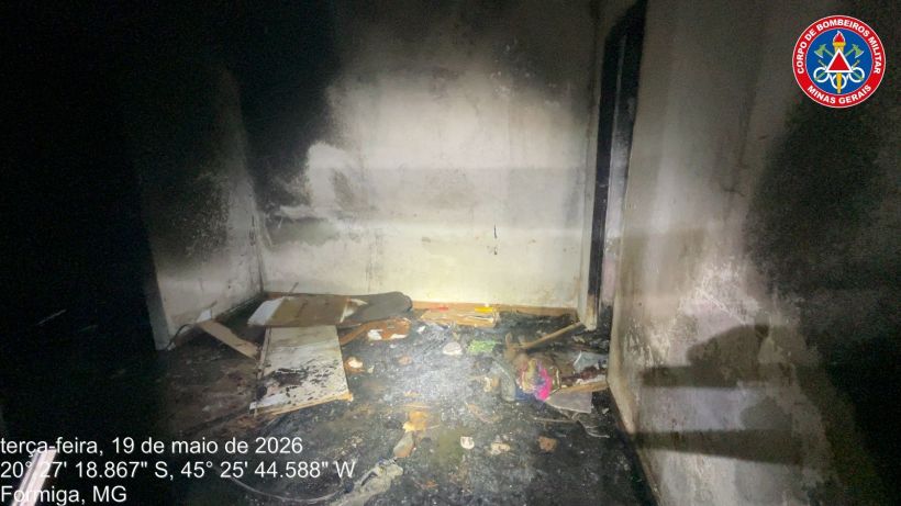 Interior de um cômodo com paredes danificadas e lixo espalhado, mostrando os sinais de um incêndio. Data: 19 de maio de 2026, local: Formiga, MG.