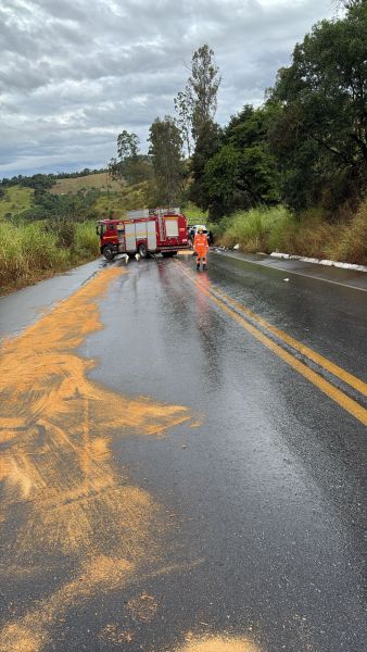 Caminho molhado com uma caminhonete de bombeiros estacionada e um trabalhador de segurança em trajes laranja, enquanto um material em pó alaranjado está espalhado na estrada.