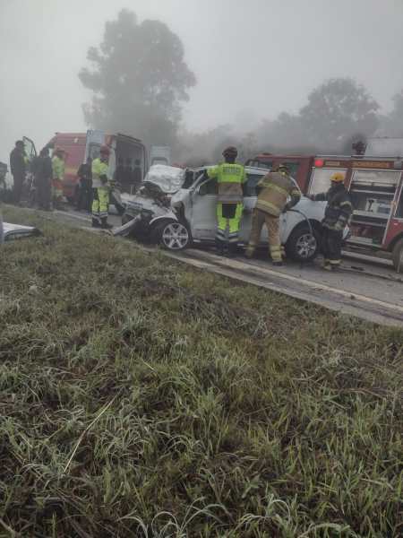 Grupo de socorristas trabalhando em um acidente de trânsito em uma estrada com neblina, realizando o resgate de ocupantes em um carro danificado.