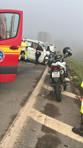 Acidente de trânsito em uma estrada com visibilidade reduzida devido à neblina, envolvendo vários veículos. Equipe de resgate trabalhando na cena.