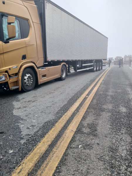 Caminhão amarelo parado em uma estrada com neblina, com caixa de transporte acoplada atrás.