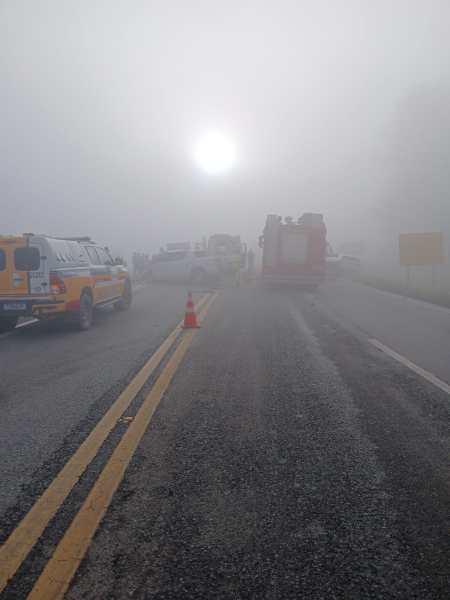 Cenas de uma estrada coberta por névoa densa com veículos parados ao fundo, incluindo carros de bombeiros, e um sol fraco visível através da neblina.