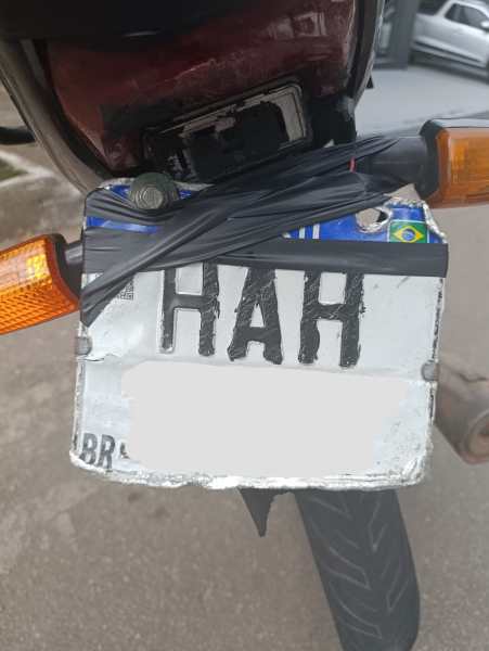 Placa de motocicleta com as letras 'HAH' visíveis, fixada com fios preto em um suporte.