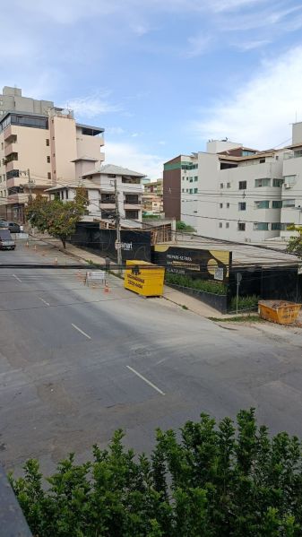 Vista de uma rua com edifícios residenciais e comerciais ao fundo, cercada por obras e barreiras de segurança.
