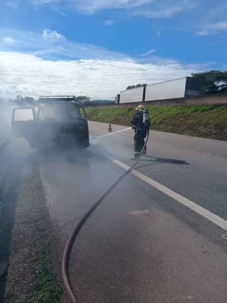 Bombeiro apagando incêndio em veículo na estrada, com fumaça saindo do carro.