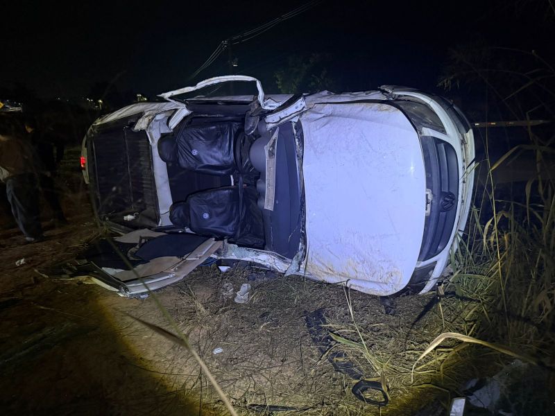 Carro capotado em um terreno à noite, com um lado virado para cima e bancos visíveis dentro do veículo.