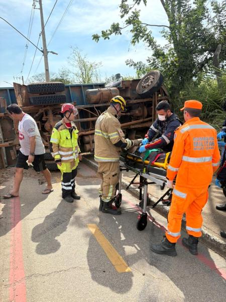 Cerca de um acidente de trânsito com um caminhão tombado, equipes de resgate e bombeiros prestando atendimento a uma vítima, incluindo profissionais em uniformes de emergência.