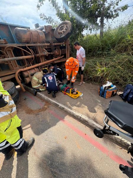 Acidente de caminhão tombado com equipes de resgate atendendo uma pessoa ferida na estrada.