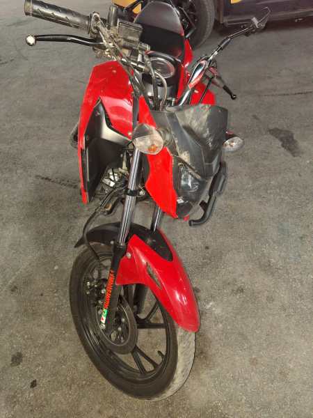 Moto vermelha em fundo de piso de concreto, vista frontal, com detalhes do guidão e roda dianteira visíveis.