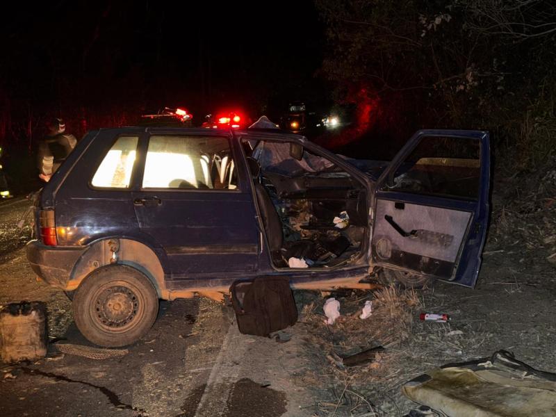 Carro acidentado na estrada à noite, com porta aberta e danos visíveis.